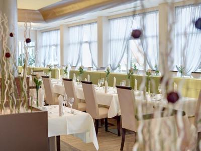 Helles Restaurant mit großen Fenstern, weißen Tischdecken und beigen Stühlen in ordentlicher Reihenfolge.