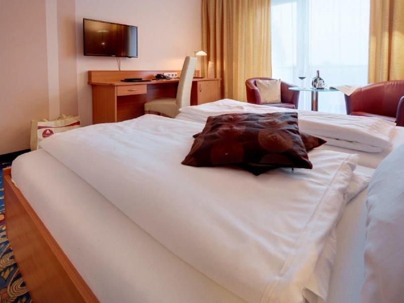 Przytulny pokój hotelowy z dużym łóżkiem, biurkiem i fotelami przy oknie.