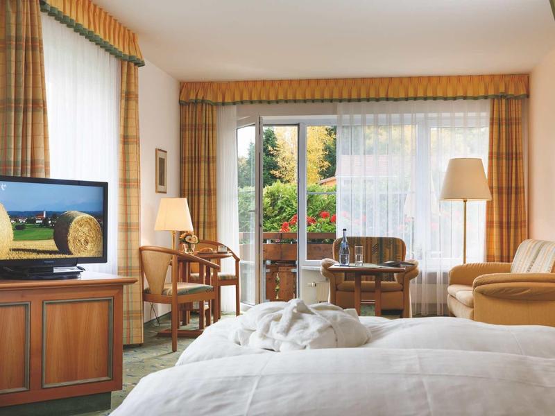 Camera d'hotel accogliente con letto matrimoniale, area salotto e vista su balcone con giardino.