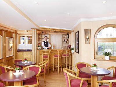 Cozy hotel bar with wooden furniture and bartender behind the counter.