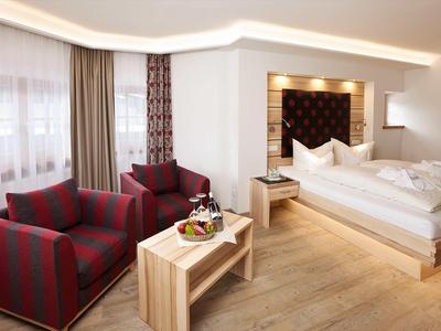 Modern eingerichtetes Hotelzimmer mit Doppelbett, zwei Sesseln und Holzmöbeln.