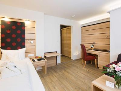 Bright hotel room with single bed, desk, red chair, and flowers on the table.