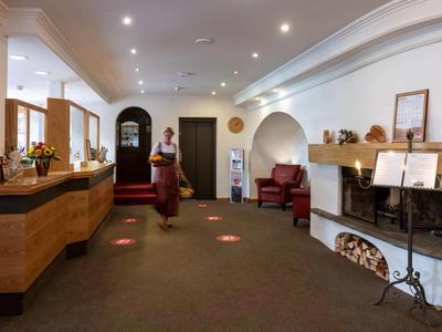 Helle Hotellobby mit Rezeption, Kamin und Sitzbereich, eine Frau trägt traditionelle Kleidung.