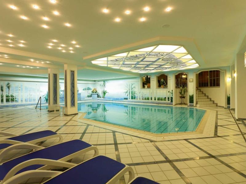 Indoor pool with lounge chairs and bright skylight in a hotel.