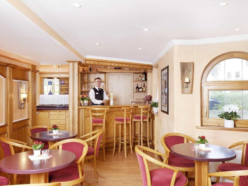 Cozy hotel bar with wooden furniture and bartender behind the counter.