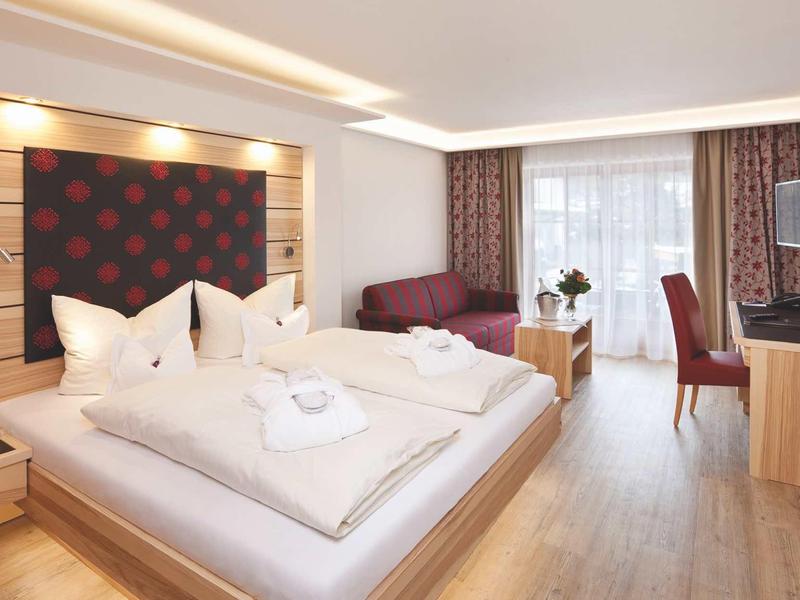 Modern hotel room with double bed, seating area, and desk.