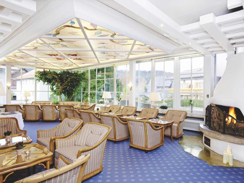 Bright conservatory with wicker armchairs, fireplace, blue carpet, and large windows.