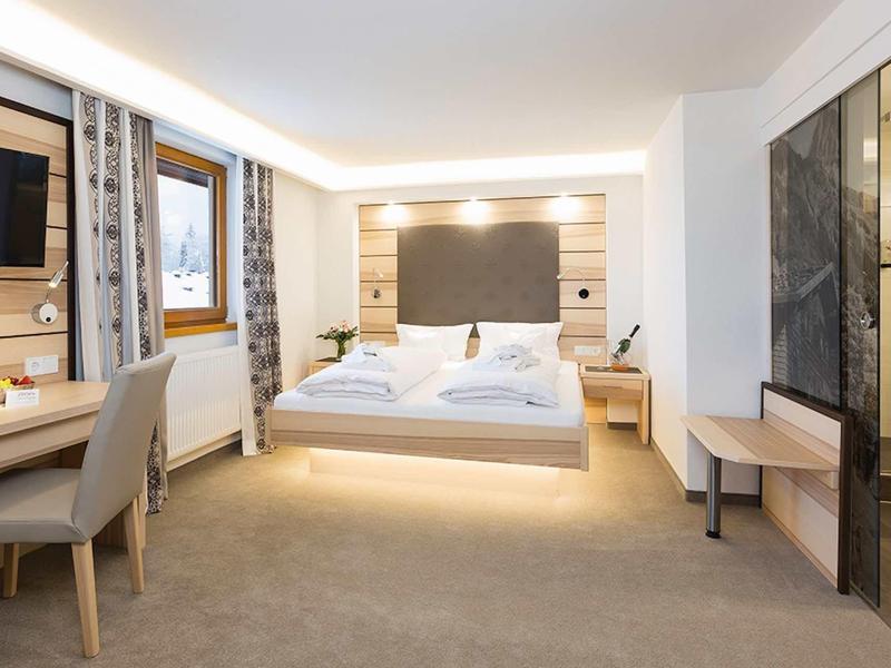 Modern hotel room with double bed, desk, TV, and glass-door shower.