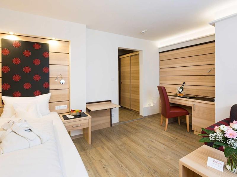 Bright hotel room with single bed, desk, red chair, and flowers on the table.