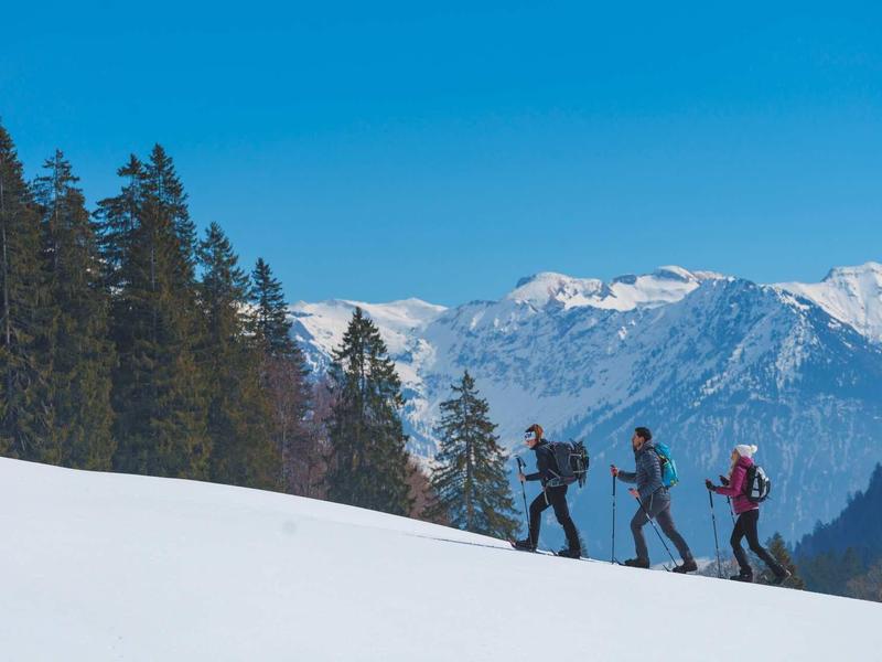 Three hikers with backpacks walking in a snowy mountain area under a clear blue sky.