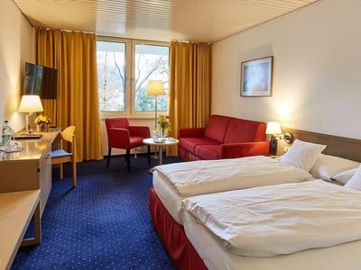 Chambre d'hôtel confortable avec deux lits simples, canapé rouge et moquette bleue.