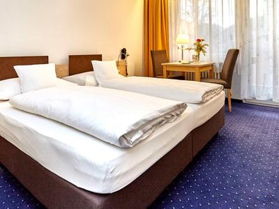 Chambre d'hôtel avec deux lits simples, tapis bleu et rideaux jaunes près d'une fenêtre.