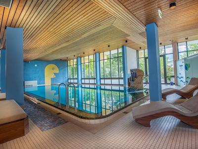 Piscine intérieure avec plafond en bois, grandes fenêtres et chaises longues dans un hôtel.