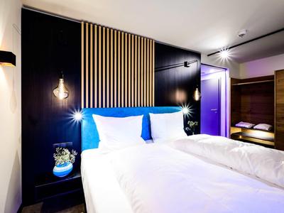 Modernes Schlafzimmer mit großem Bett, weißen Bettwäsche, Holzpaneelen und sanfter Beleuchtung.