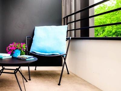 Moderner Balkon mit schwarzem Stuhl, blauem Kissen, runden Tischen und buntem Blumenarrangement.