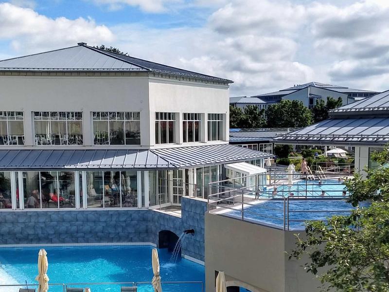 Außenpoolbereich mit Liegestühlen, hellen Gebäuden und Wolkenhimmel im Hintergrund.