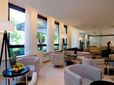 Chambre d'hôtel lumineuse et moderne avec fauteuils gris, grandes fenêtres et plantes.