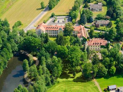 Luftaufnahme eines Hotels umgeben von Bäumen, nahe einem Fluss und landwirtschaftlichen Feldern.
