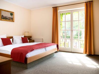 Hell eingerichtetes Hotelzimmer mit großem Doppelbett und französischem Fenster