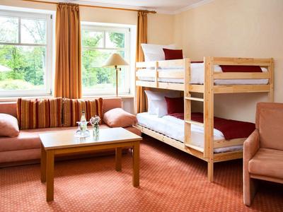 Gemütliches Zimmer mit Etagenbett, Sofa, Sesseln und großem Fenster mit Vorhängen.