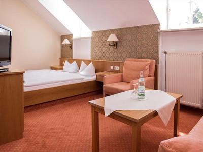 Gemütliches Hotelzimmer mit Doppelbett, Sessel, Tisch und Fernseher unter Dachschräge.