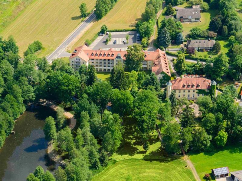 Vue aérienne d'un hôtel entouré d'arbres verts et d'une rivière en zone rurale.