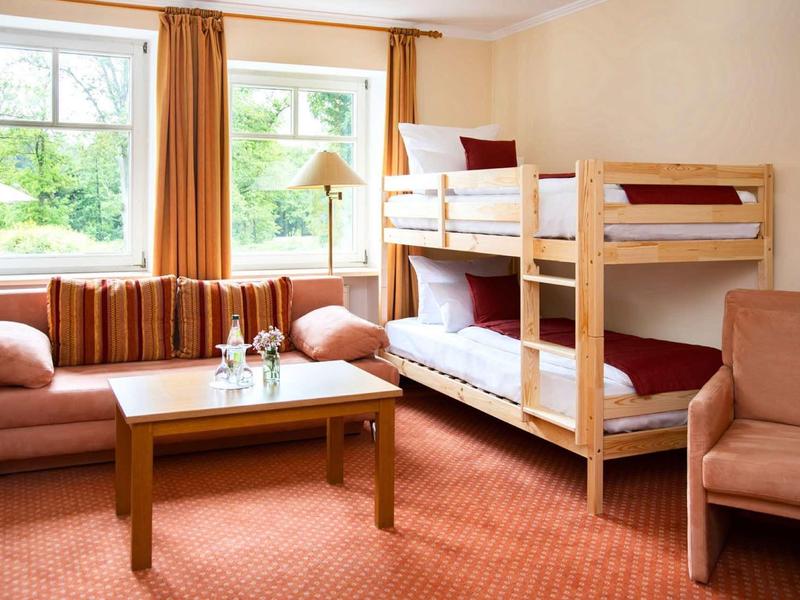 Chambre d'hôtel confortable avec lits superposés, canapé, fauteuil et fenêtre avec rideaux.