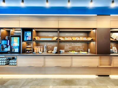 Moderní hotelový bar s osvětleným bufetem a kávovarem pod modrým osvětlením.