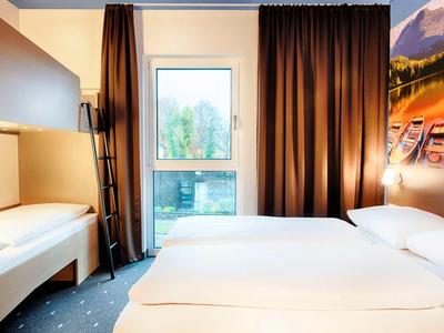Modernes Hotelzimmer mit Doppelbett, Sitzbank, dunklen Vorhängen und Landschaftsbild an der Wand.