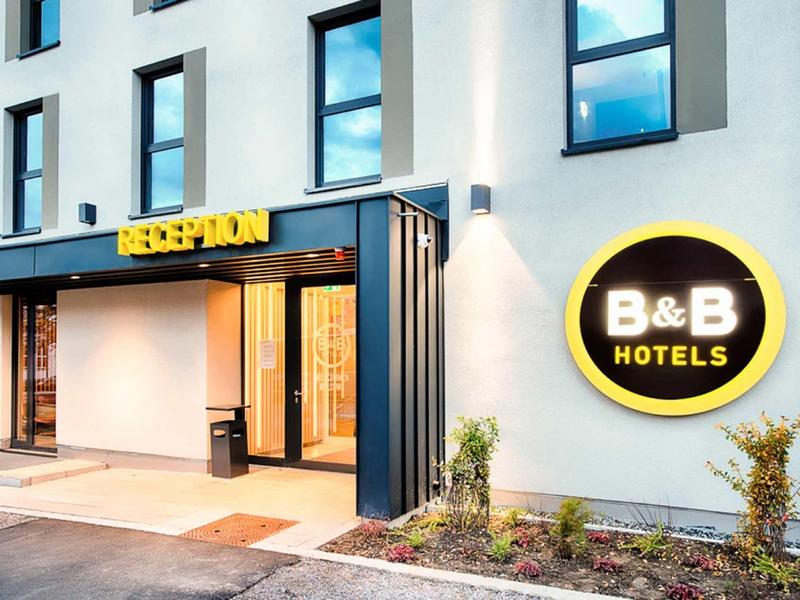 Moderne Hotel-Fassade mit großen Fenstern, schwarzem Eingangsbereich und gelbem B&B Hotels-Logo.