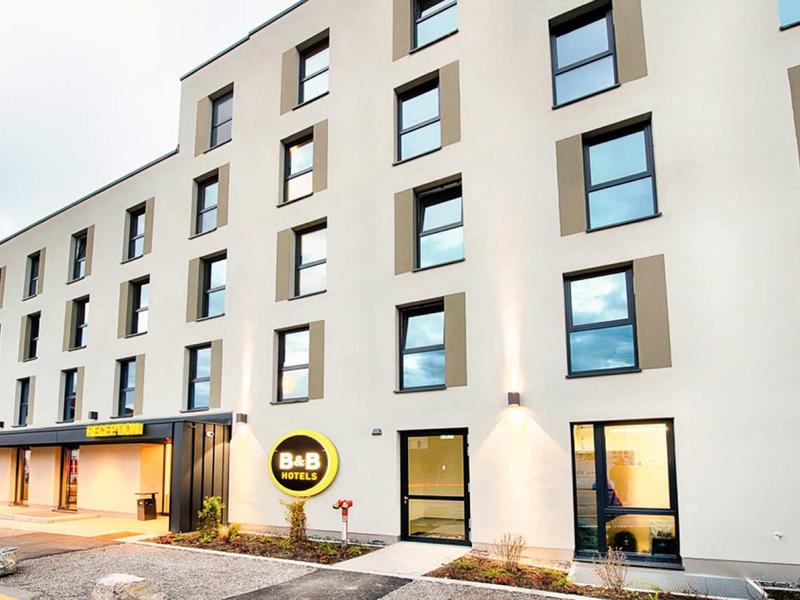 Moderner, weißer Gebäudekomplex mit großen Fenstern und flachem Dach, Eingang mit Glasfront.