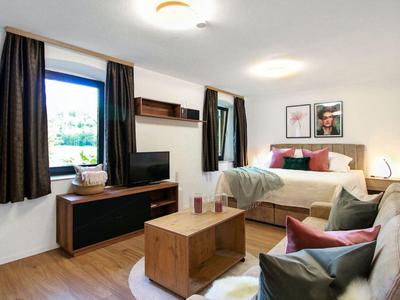 Gemütliches Wohnzimmer mit Sofa, Fernseher, Holzkommode und Bettnische in hellem, modernem Stil.