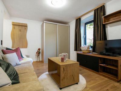 Helles Wohnzimmer mit Holzmöbeln, Sofa, Fernseher und Vorhängen an einem Fenster.