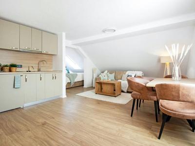 Helles Wohnzimmer mit Holzboden, Sofa, Essbereich und kleiner Küchenzeile unter Dachschräge.