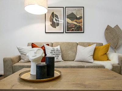 Wohnzimmer mit grauem Sofa, bunten Kissen und moderner Dekoration auf dem Holztisch.