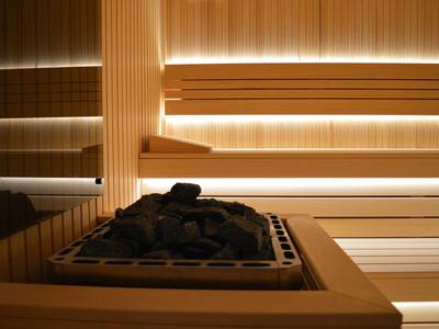Moderne Sauna mit Holzbank, warmem Licht und einem Ofen mit schwarzen Saunasteinen.