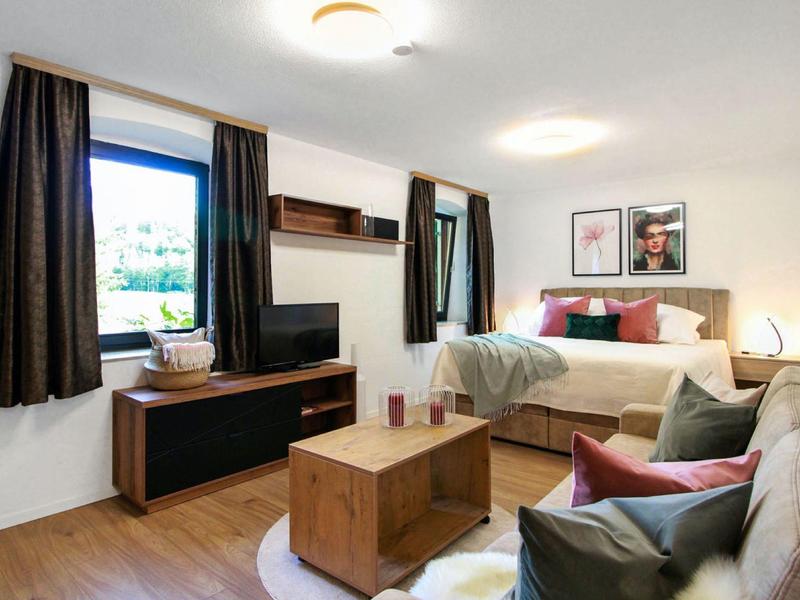 Gemütliches Wohnzimmer mit Sofa, Fernseher, Holzkommode und Bettnische in hellem, modernem Stil.