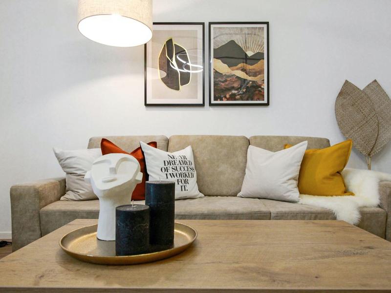 Moderner Wohnbereich mit grauem Sofa, bunten Kissen und Holztablett auf Tisch im Vordergrund.