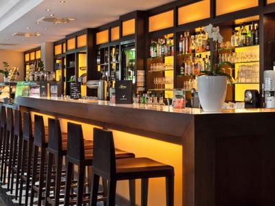 Moderne hotelbar met hoge zitplaatsen, verlichte toog en grote spiegel op de achtergrond.