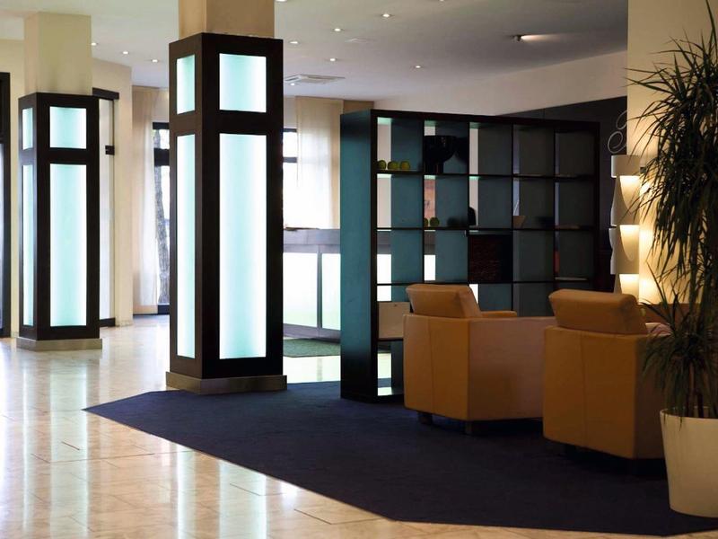 Área moderna de lobby de hotel con sillones cómodos, grandes ventanas y columnas de iluminación decorativas.