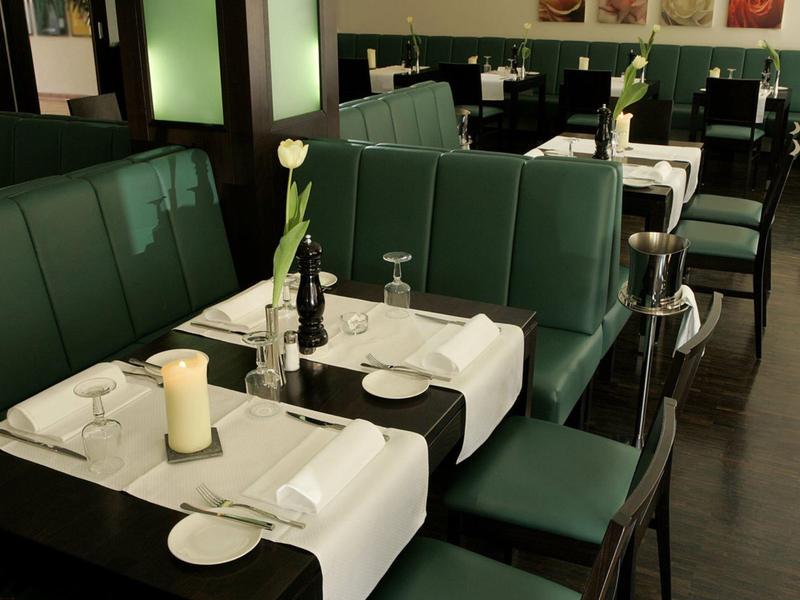 Restaurante elegante con asientos verdes, manteles blancos y decoración de mesa para huéspedes.