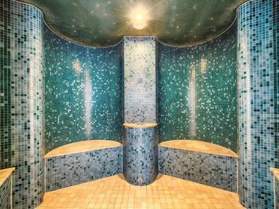 Ronde wellnessruimte met groene mozaïekwanden en ingebouwde banken.