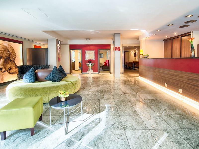 Lichte hotel lobby met groene bank, marmeren vloer en rood receptiebalie