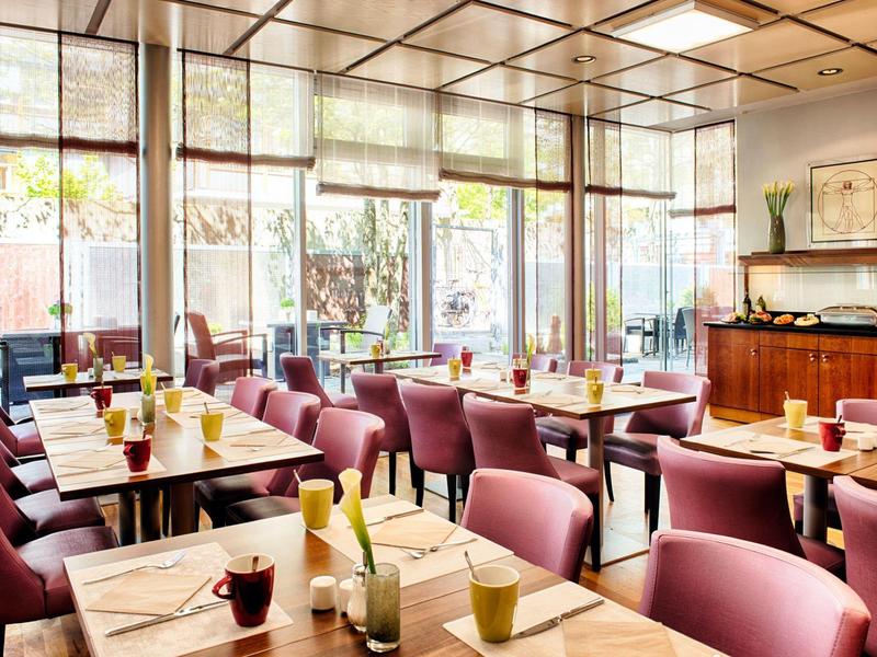 Lichte ontbijtruimte met tafels, comfortabele stoelen en grote ramen.