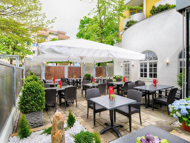Terras met tafels, stoelen en parasols naast een hotelgebouw, versierd met planten.