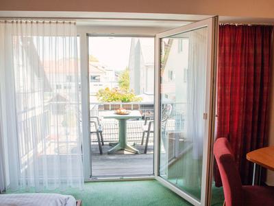 Widok przez otwarte drzwi balkonowe z dwoma krzesłami i stołem na zewnątrz.