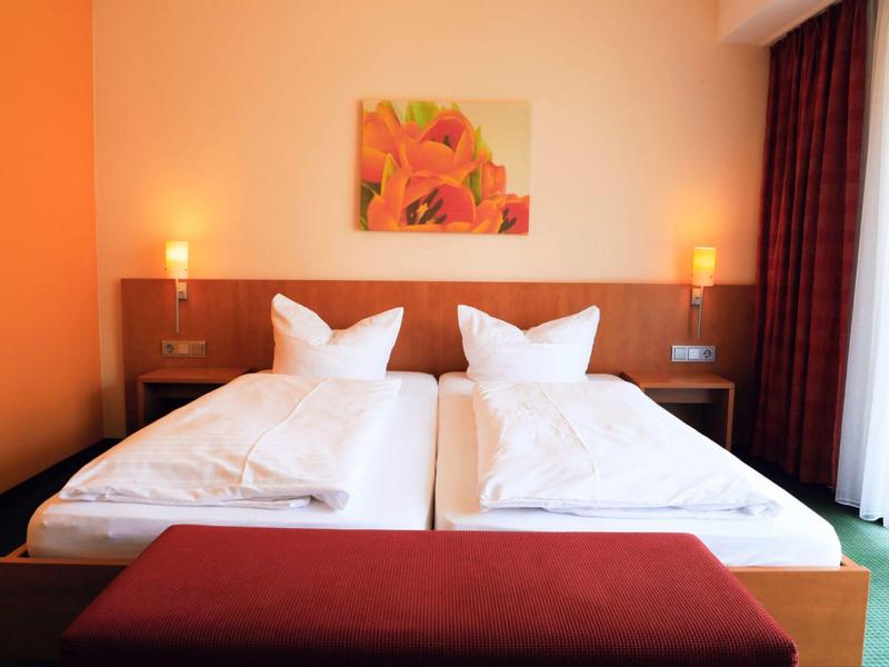 Jasny pokój hotelowy z dwoma pojedynczymi łóżkami, lampkami nocnymi i obrazem na ścianie.