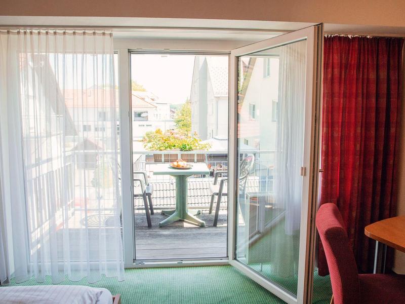 Widok przez otwarte drzwi balkonowe z dwoma krzesłami i stołem na zewnątrz.