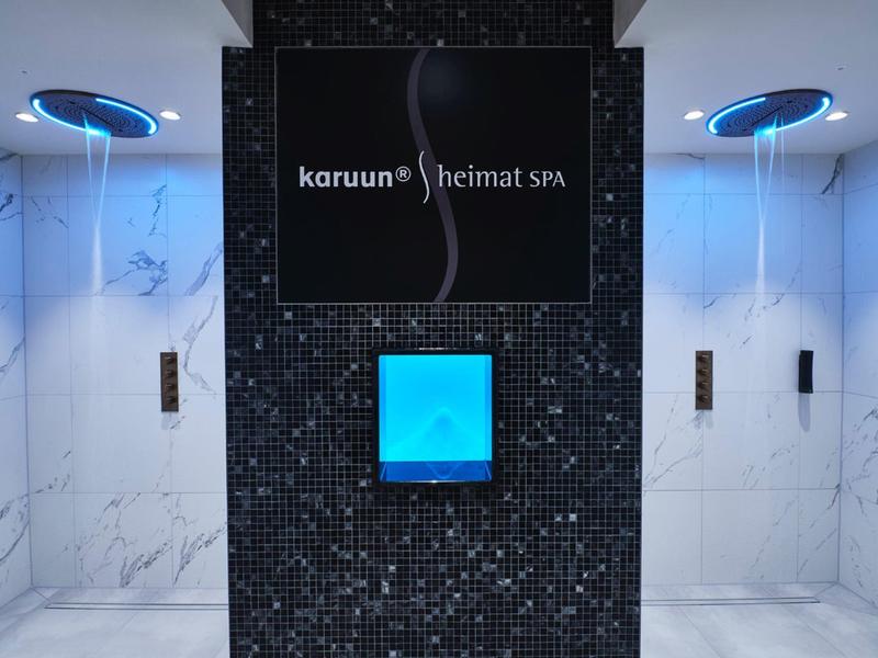 Dwie windy z niebieskim oświetleniem w nowoczesnym hotelu z kafelkową ścianą między nimi.