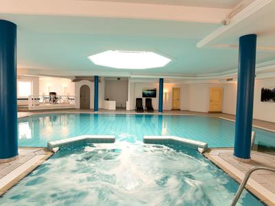 Binnenzwembad met bubbelbad, blauwe pilaren en helder dakraam in een hotel.